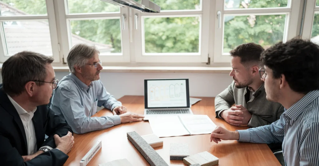 Beratungsgespräch am Besprechungstisch mit Sanierungsfahrplan auf dem Bildschirm und Dämmstoffmustern auf dem Tisch