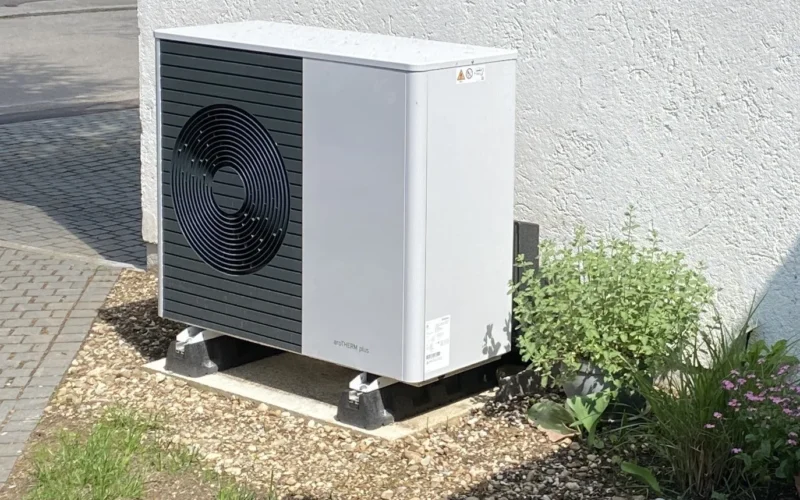 Luft-Wärmepumpe als Außeneinheit auf einem Kiesbett neben einem Wohnhaus