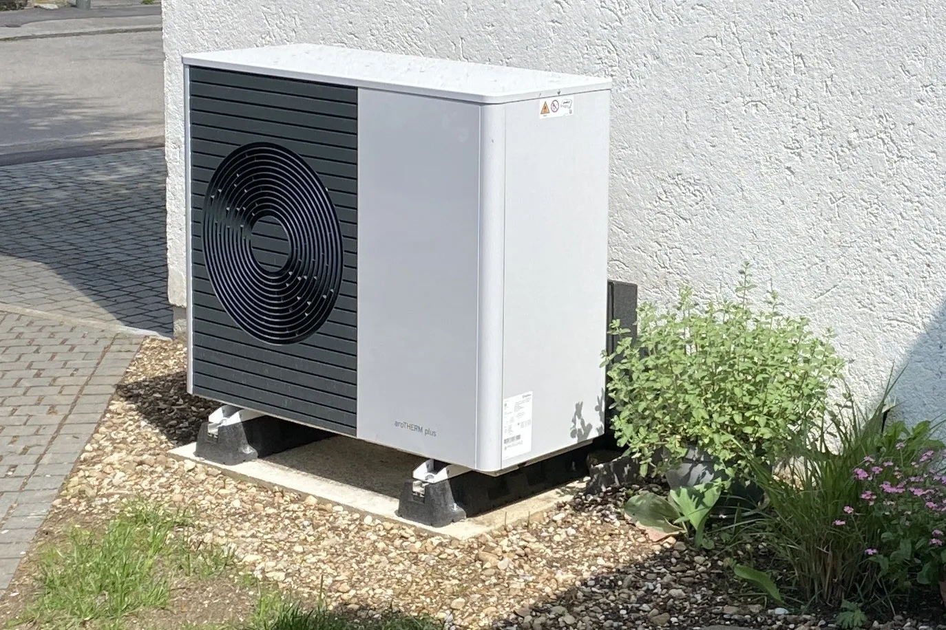 Luft-Wärmepumpe als Außeneinheit auf einem Kiesbett neben einem Wohnhaus