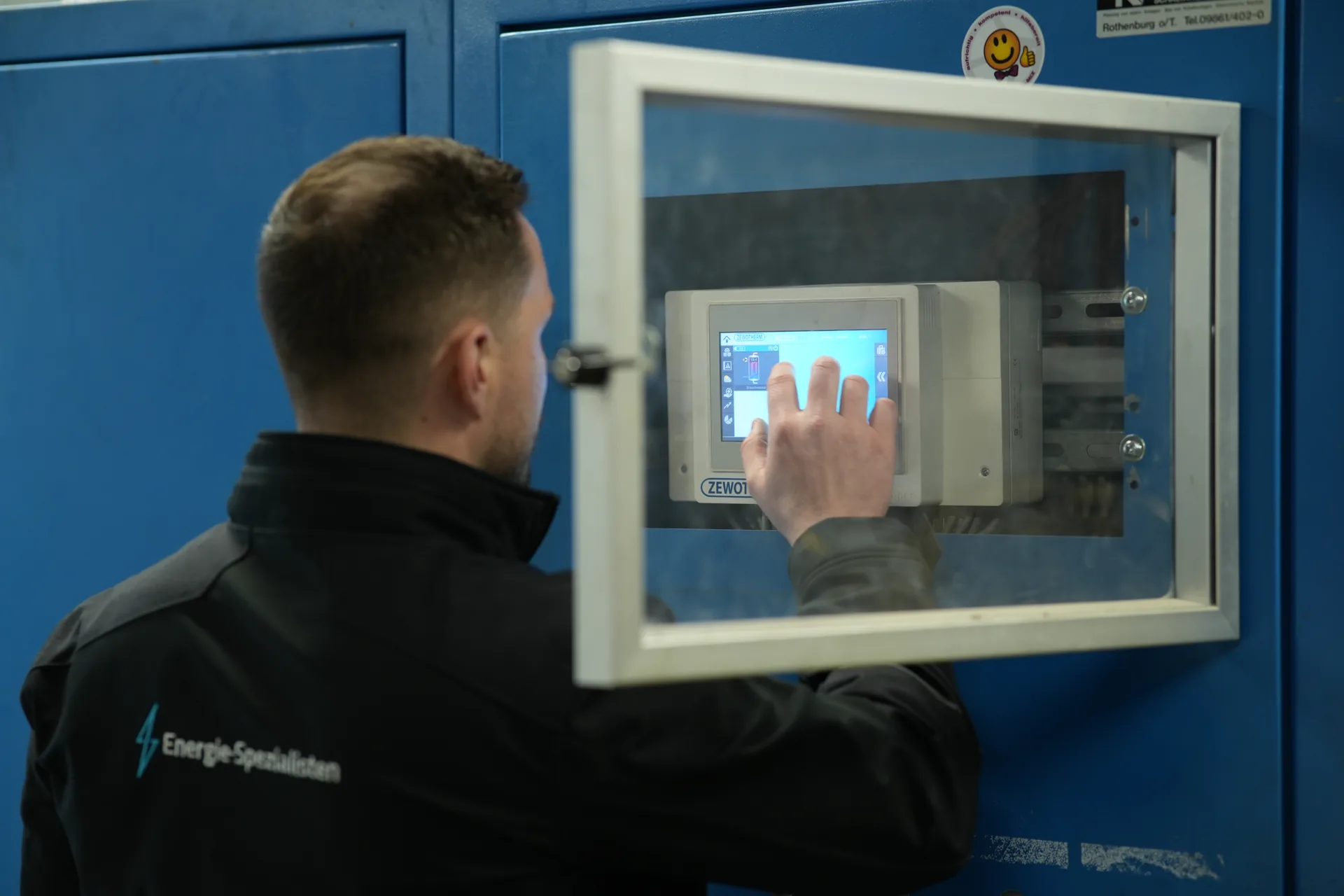 Energieberater stellt die Regelung einer Heizungsanlage am Touchdisplay im Schaltschrank ein