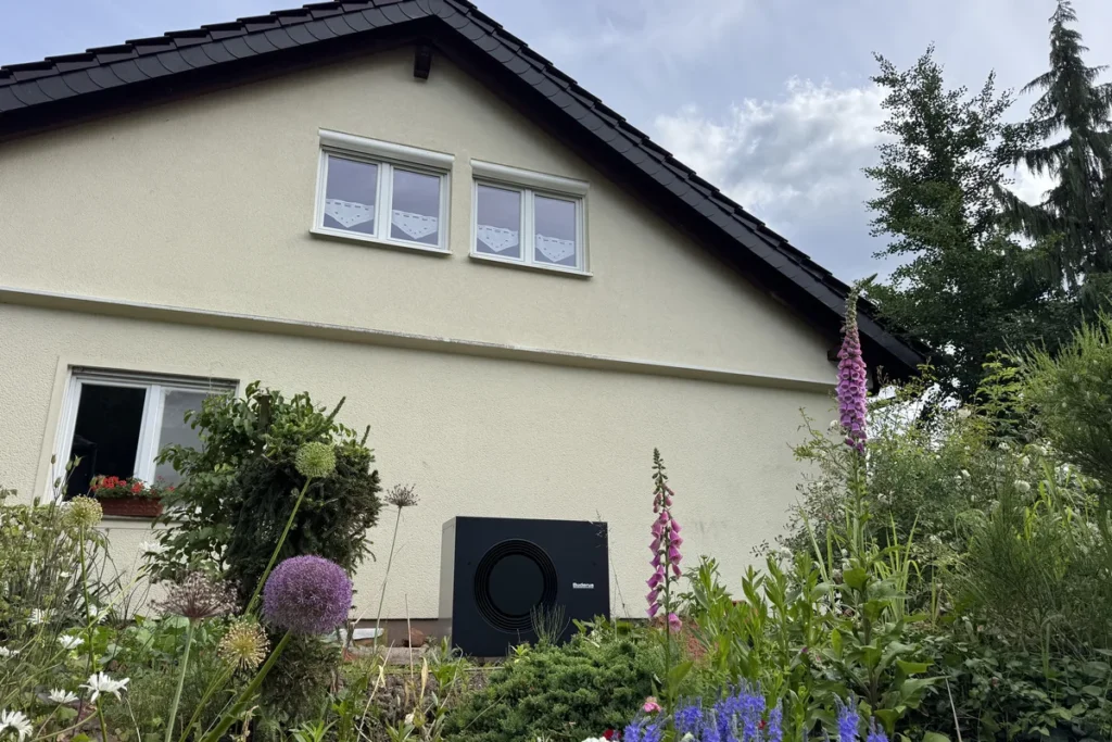 Einfamilienhaus mit Luft-Wärmepumpe an der Giebelseite, davor ein blühender Staudengarten